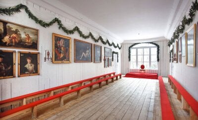 Rikssalen i Eidsvollsbygningen med røde benker, plankevegger og malerier på veggene