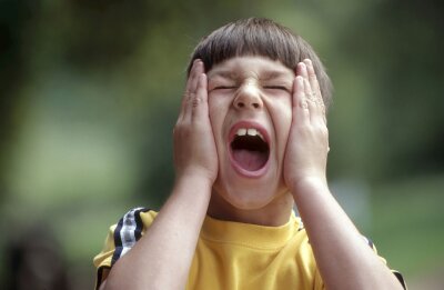 En gutt holder hendene på kinnene og skriker med åpen munn og lukkede øyne.