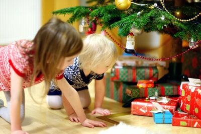 To barn sitter på kne og ser på julegavene som ligger under juletreet. 