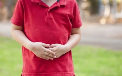 Et barn i rød t-skjorte som holder seg på magen.