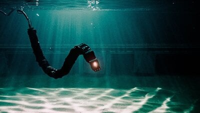 Bilde av slangeroboten som svømmer under vann, med en lampe i front.