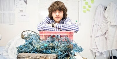Bilde av Boyan Slat som lener seg over avfall som er funnet i havet. 