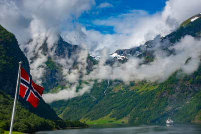 Bilde av det norske flagg, med norsk natur, fjell og fjord om sommeren i bakgrunnen 