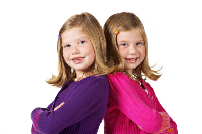 To tvillinger står med armene i kors og ryggen mot hverandre, mens de smiler mot kameraet.