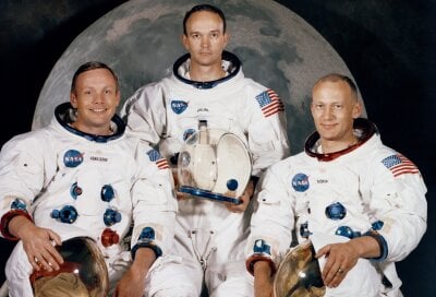 Tre astronauter sitter med sine romdrakter klare til å dra ut i verdensrommet