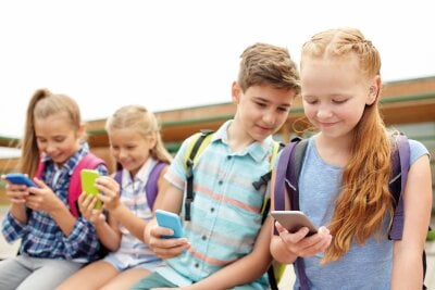 4 barn sitter i skolegården og ser på mobilene sine. 