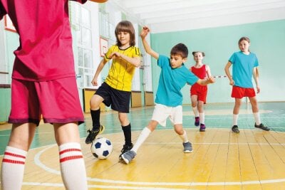 Barn spiller fotball inne i en gymsal på skolen.