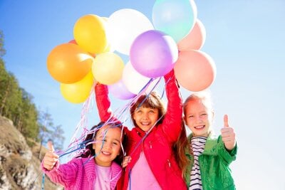 Tre jenter står ute og holder mange ballonger opp i været