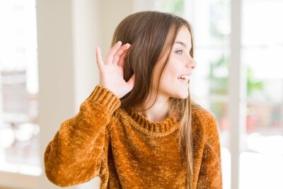 En jente holder den ene hånden opp mot øret og lytter til lyder