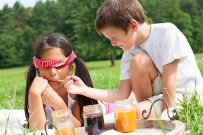 To barn sitter ute og gjør en smakstest på syltetøy, den ene har bind foran øynene.