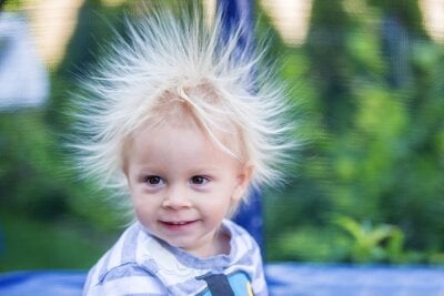 En liten gutt med lyst hår har hårstrå stående til alle kanter som følge av statisk elektrisitet